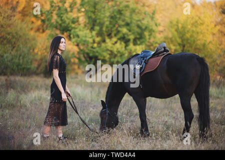 Bella donna in piedi vicino a cavallo e tenendo le piogge in autunno park. Foto Stock