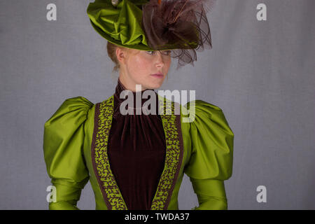 Late Victorian donna che indossa una seta verde ensemble e un cappello di grandi dimensioni Foto Stock