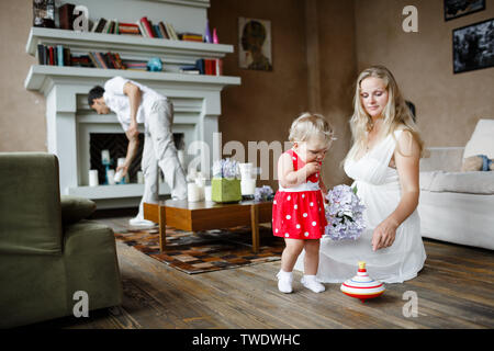 Donna incinta in abito bianco che gioca con un anno di età bambino seduto su un pavimento Foto Stock