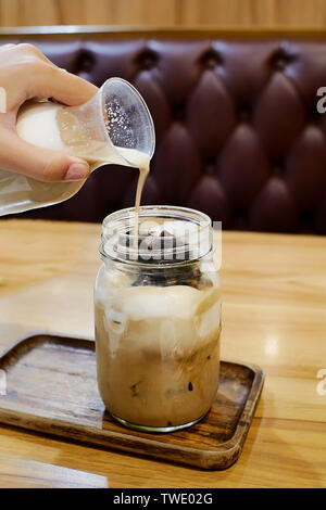 Versare il latte nel caffè freddo in una caffetteria. Foto Stock