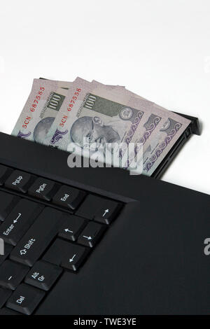 Computer portatile con centinaia di rupie banconote Foto Stock