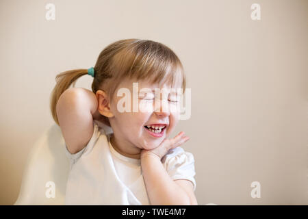 Poco ridere kid Caucasian ragazza con gli occhi chiusi carino closeup faccia su sfondo semplice Foto Stock