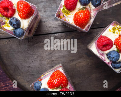 Tazze di lamponi, more fragole servite con noci e panna montata su un vecchio tavolo di legno. Vista dall'alto. Immagine quadrata Foto Stock