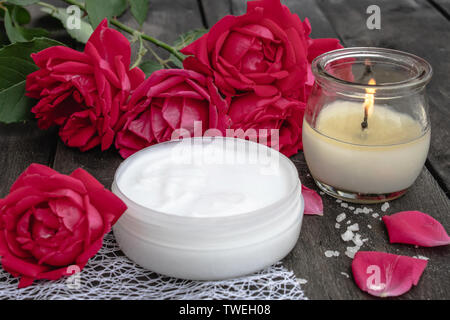 Crema cosmetica e rose con petali di fiori e una candela che brucia sul vecchio sfondo di legno. close-up Foto Stock