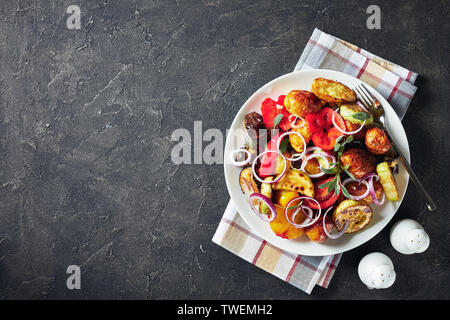 Appena tostato in un forno caldo verdure - patate e melanzane, zucchine, pomodori, peperoni su una piastra bianca su un cemento grigio tabella, vista dal Foto Stock