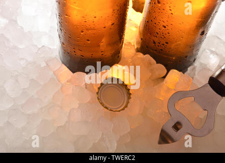 La birra di bottiglie di vetro su ghiaccio con cappuccio e apribottiglie . Composizione orizzontale. Vista in elevazione. Foto Stock