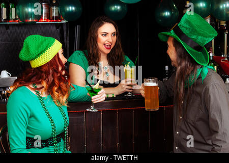 La compagnia di ragazze giovani e un uomo di celebrare la festa di San Patrizio. Essi hanno divertimento presso il bar. Essi sono vestiti di Carnevale copricapo Cappelli verde e cl Foto Stock