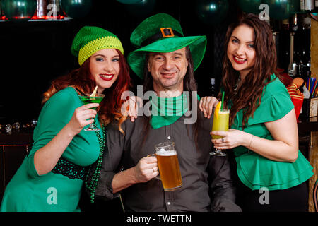 La compagnia di ragazze giovani e un uomo di celebrare la festa di San Patrizio. Essi hanno divertimento presso il bar. Essi sono vestiti di Carnevale copricapo Cappelli verde e cl Foto Stock