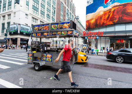 La città di New York, Stati Uniti d'America - 31 Luglio 2018: uomo che porta un carrello del cibo su una strada con enormi schermi pubblicitari e la gente intorno a Manhattan, New York City, Foto Stock