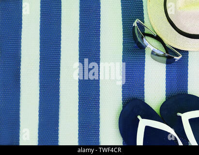 Cappello di paglia di occhiali da sole e pantofole su un tappetino con striping Foto Stock
