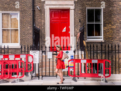 Donna che indossa red oltrepassando porta rossa con red roadworks segno a Londra. Foto Stock