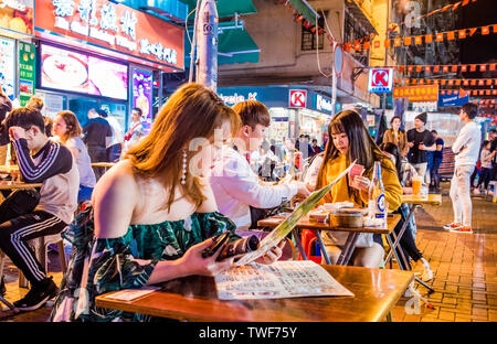 Un folto gruppo di persone rilassarsi e socializzare presso il Mercato Notturno di Temple Street a Hong Kong. Foto Stock