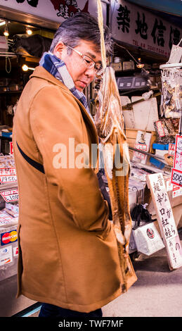 Uomo che guarda le merci presso il Mercato del Pesce di Tsukiji a Tokyo in Giappone. Foto Stock