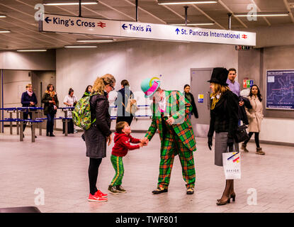 Un giovane bambino con sua madre si stringono la mano con uomo vestito con una tuta da clown in stazione metropolitana di Kings Cross a Londra. Foto Stock