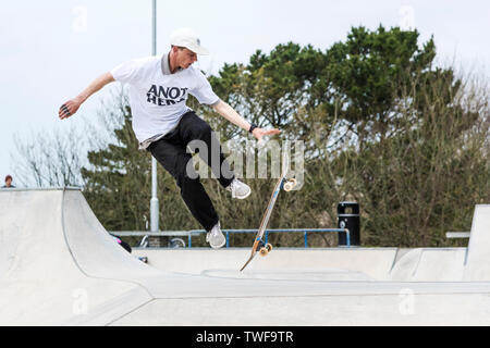 Un guidatore di skateboard tenta un trucco di antenna a onde Concrete Skate Park a Newquay in Cornovaglia. Foto Stock