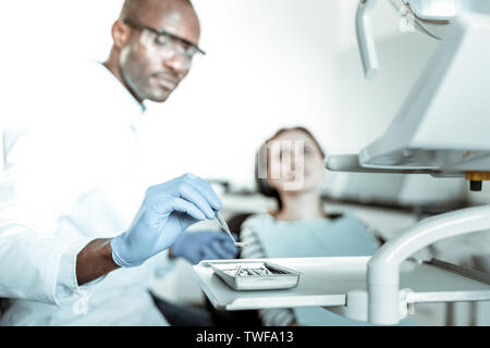 Osservando la cavità orale. Di carnagione scura accurata medico e la sua paziente di sesso femminile avente checkup in completamente accessoriate cabinet Foto Stock