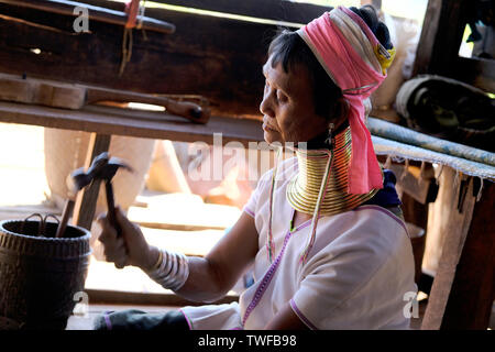 Un lungo collo tribù Karen donna usa un martello per fare gioielli nello Stato di Kayah in Myanmar. Foto Stock