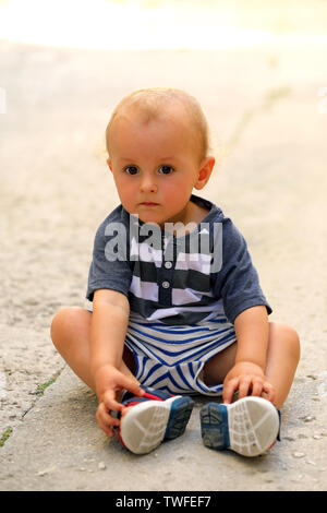 Carino bambino seduto sul pavimento in strada, Close Up ritratto Foto Stock