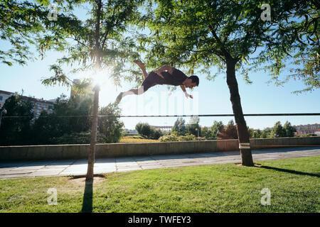Metà adulto uomo caucasico jumping e camminare sulla corda appesa su alberi, facendo un lavoro trickline fuori di routine in Madrid, Spagna. Foto Stock
