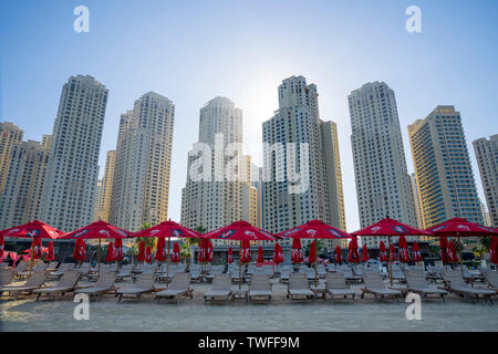 Le torri residenziali si elevano al di sopra dei filari di sedie da spiaggia di Jumeirah Beach in Dubai. Foto Stock