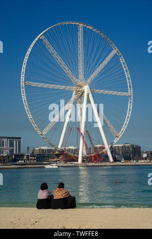 Due donne sulla spiaggia di Jumeirah a Dubai si affacciano sull'acqua e ruota panoramica Ferris in costruzione. Foto Stock