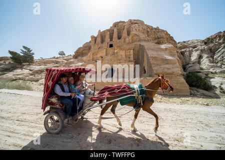 Un carrello di beduino con ansiosa i turisti trot oltre un secolo prima tomba a Petra in Giordania. Foto Stock