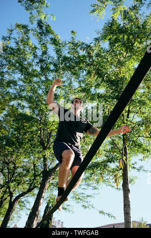 Metà adulto uomo caucasico jumping e camminare sulla corda appesa su alberi, facendo un lavoro trickline fuori di routine in Madrid, Spagna. Foto Stock