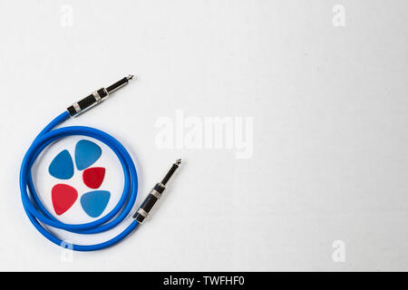 Chitarra blu cavo patch su uno sfondo bianco con rosso bianco e blu picks. Lo sfondo bianco ha copyspace. Il cavo è per una chitarra elettrica o Foto Stock