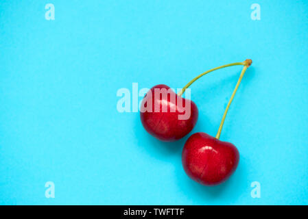 Due rosso ciliegia matura beries su sfondo blu. Lay piatto. Cibo sano concetto. Foto Stock