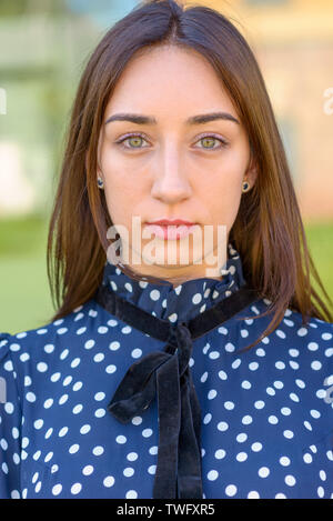 Grave giovane elegante blu-eyed donna che indossa un blu e bianco polka dot dress fissando attentamente la fotocamera in una stretta su ritratto Foto Stock