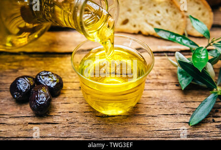 Organici pressato a freddo Olio d'oliva italiano. Bottiglia versando olio d'oliva vergine in una ciotola close up Foto Stock