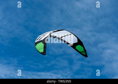 Il bianco e il verde kitesurf il traino di kite in aria con un cielo blu come sfondo Foto Stock
