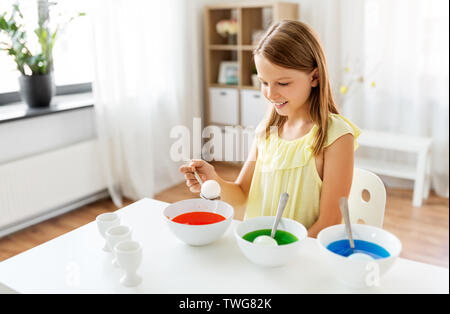 Ragazza colorare le uova di pasqua dal liquido di tintura a casa Foto Stock