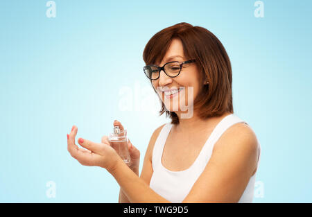 Sorridente donna senior spruzzare profumo al suo polso Foto Stock