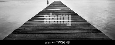 Alba di un pontile in legno che si stagliano all'oceano silenzioso in splendide in bianco e nero Foto Stock