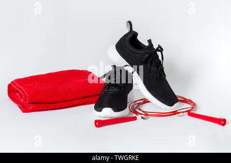 Sport nero scarpe con suola bianca, rossa salto con la corda e asciugamano rosso isolato su sfondo bianco. Concetto di fitness e uno stile di vita sano Foto Stock