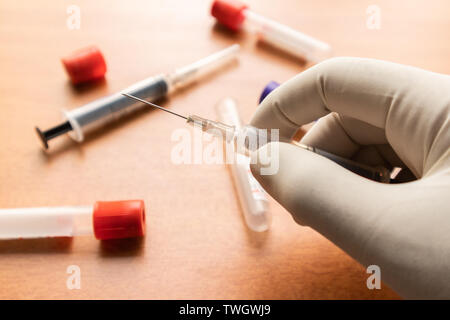 Medico mano nel guanto bianco tenendo la siringa, per ottenere un campione di sangue in laboratorio con l ausilio di pianura attivatori di coagulo come sfondo in India Foto Stock