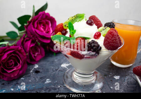 Il mandarino succo in un bicchiere, gelato alla crema con frutti di bosco sfondo. Rose Foto Stock