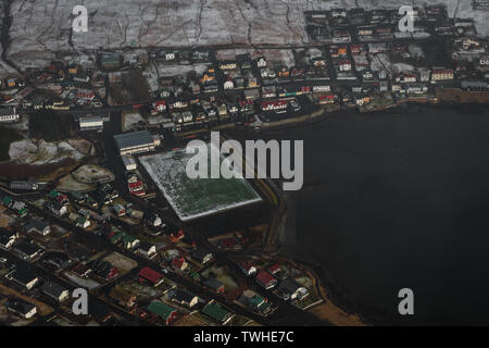 Riprese aeree del villaggio delle Isole Faeroeer Sandavagur come visto da un volo in elicottero su paesaggio innevato in primavera (Isole Faerøer) Foto Stock