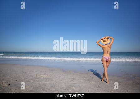 Donna in bikini e hat permanente sulla spiaggia sotto il sole Foto Stock