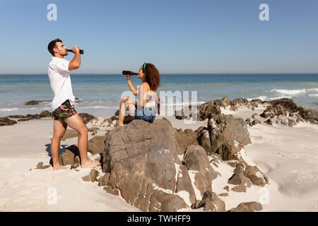 Coppia giovane bere birra sulla spiaggia sotto il sole Foto Stock