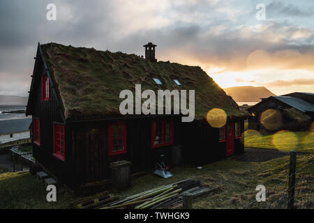 Tipico il rosso e il nero delle isole Faeroeer casa in legno con tetto di erba come avvistati durante il tramonto nel villaggio di Kirkjubour durante la primavera (Isole Faerøer) Foto Stock