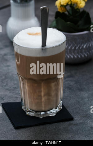 Latte macchiato di fronte un fiore giallo e zucchero sul grigio di un tavolo in un ristorante Foto Stock