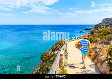 Giovane donna camminando sulla via costiera lungo mare vicino villaggio Ammopi, Karpathos Island, Grecia Foto Stock