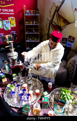 Uomo marocchino indossando un cappello di Fez versando marocchino tè alla menta al di fuori di un argento teiera, FesTeaVal 2019 al Dock di tabacco, London, Regno Unito Foto Stock
