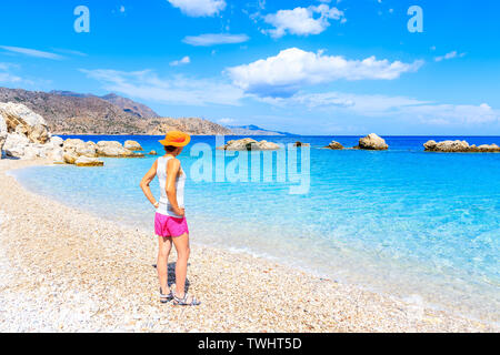 Giovane donna in piedi sulla spiaggia di Apella e guardando il mare, Karpathos Island, Grecia Foto Stock