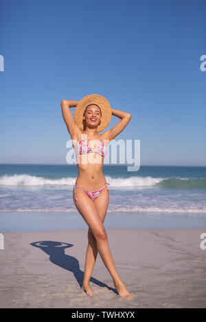 Bella donna in bikini e hat guardando la fotocamera sulla spiaggia sotto il sole Foto Stock