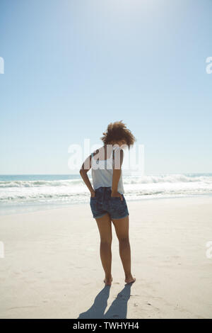 Donna in piedi con le mani in tasca sulla spiaggia Foto Stock
