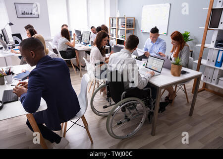 Vista laterale di un imprenditore disabili seduti sulla sedia utilizzando Laptop lavoro in ufficio Foto Stock