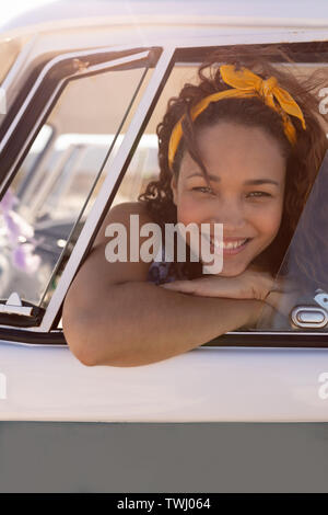 Donna birazziale che si sporge dal finestrino dell'auto, sorride Foto Stock